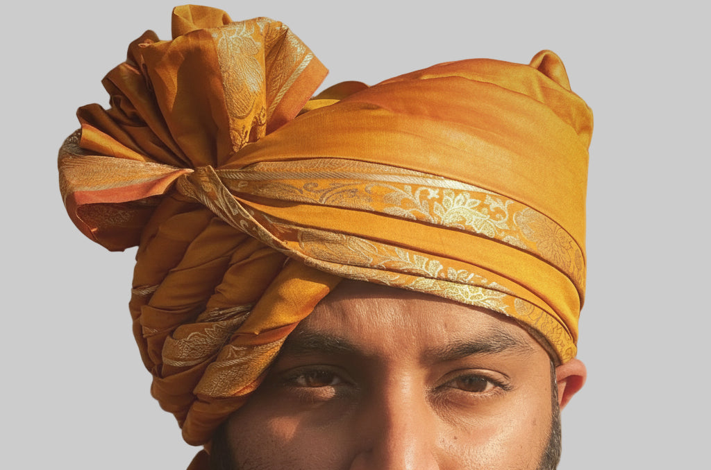 Man wearing a traditional yellow turban with intricate patterns on a plain background